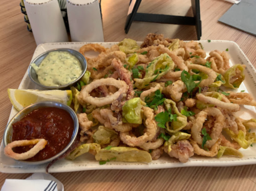 A plate of crispy calamari with dipping sauces, garnished with lettuce and lemon wedges.